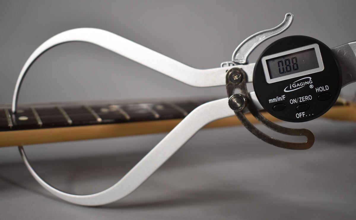 A digital caliper measures the fret height on the dark rosewood fretboard of the guitar's maple neck, showing 0.88mm.