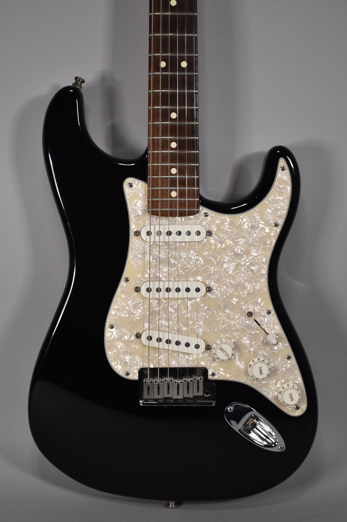 Black Stratocaster, angled from above, showing the body, pearloid pickguard, three single-coil pickups, and rosewood fretboard.