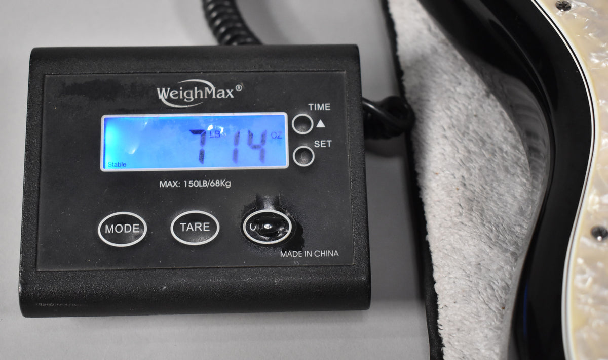 A black digital scale displays "7 LB 14 OZ" with a black Stratocaster body and pearloid pickguard on the right.