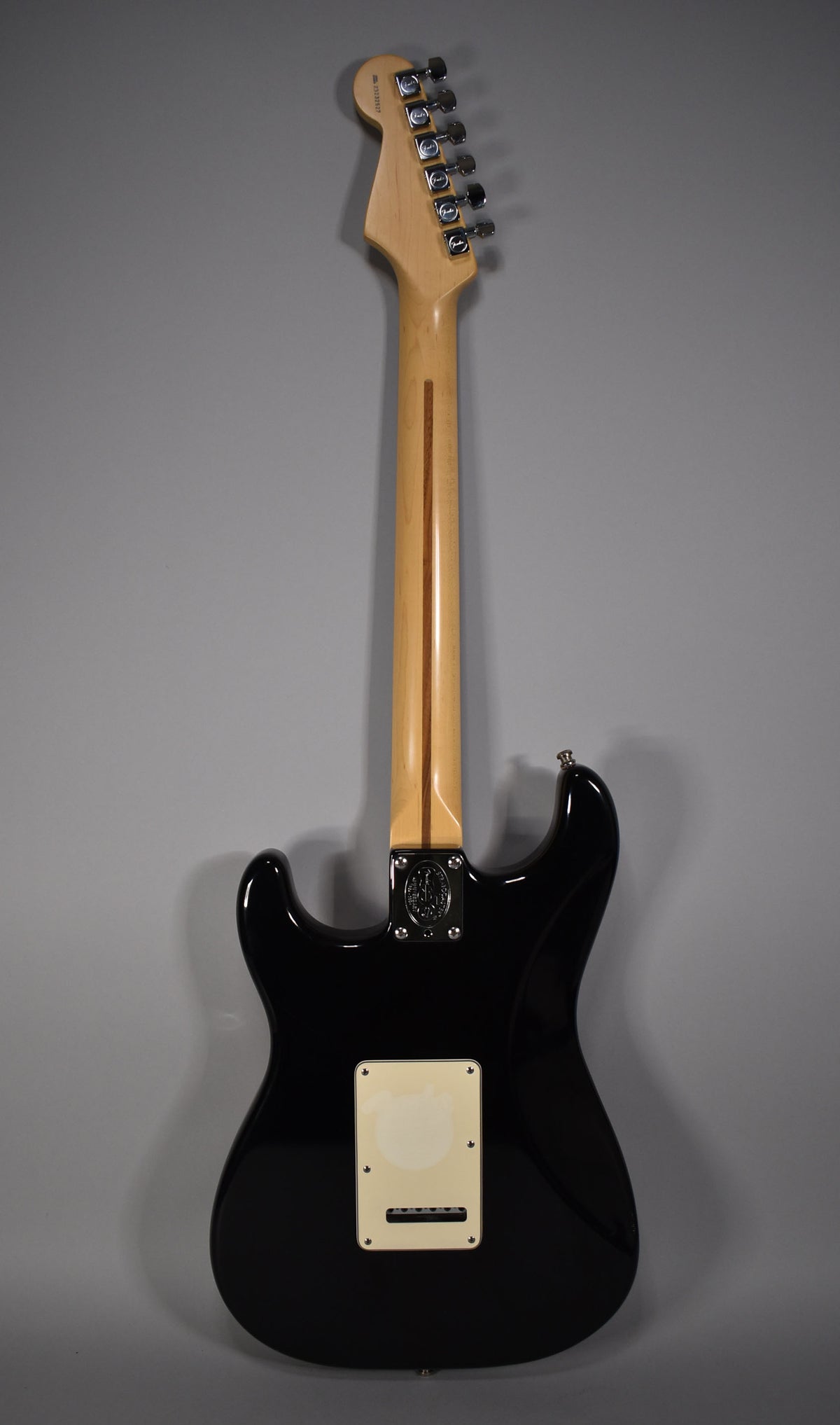 Rear view of a glossy black Stratocaster with a light maple neck, chrome tuners, and a cream-colored tremolo cover.