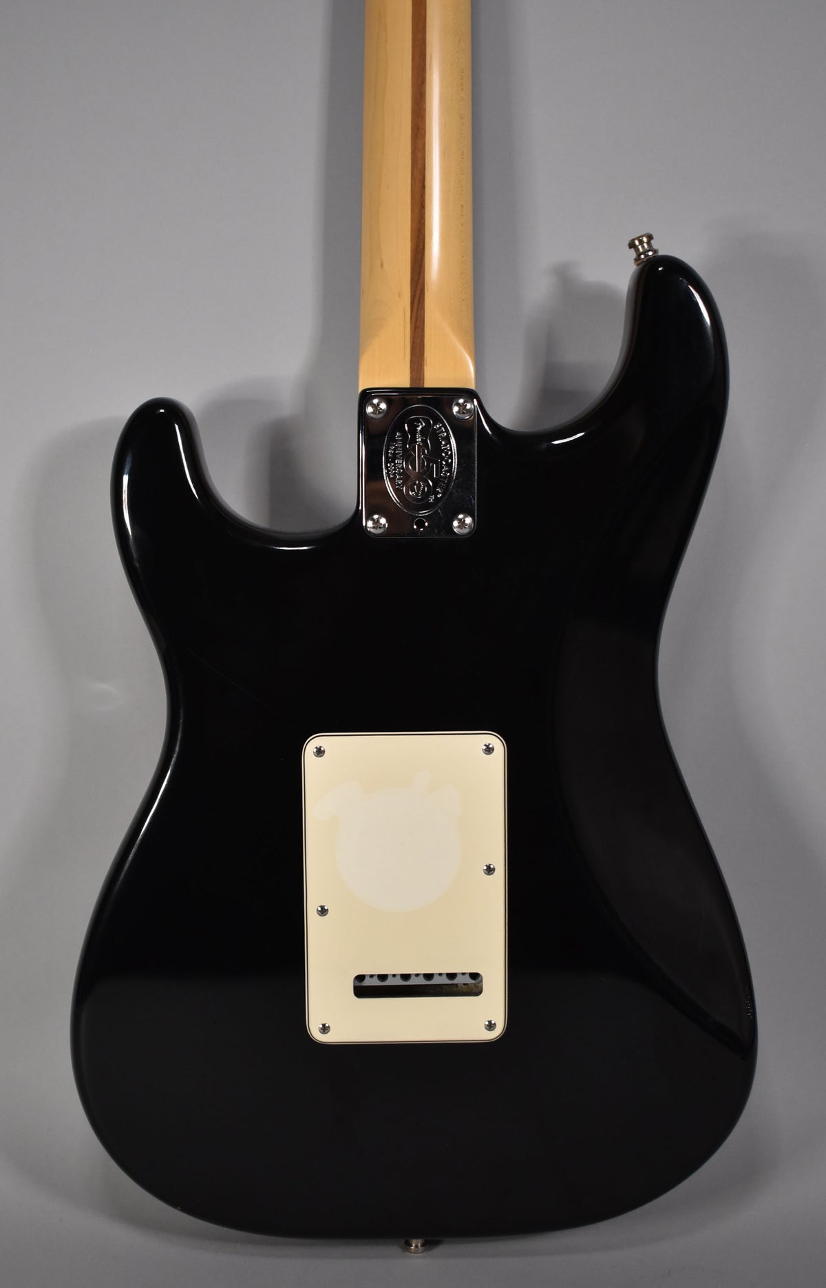 The guitar's glossy black back, with a cream tremolo cover and chrome neck plate, shows light surface scratches.