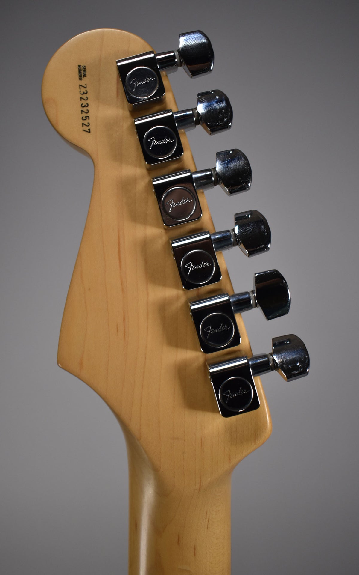 Close-up of the light wood headstock and neck heel, showing six chrome tuners and a serial number on the back.