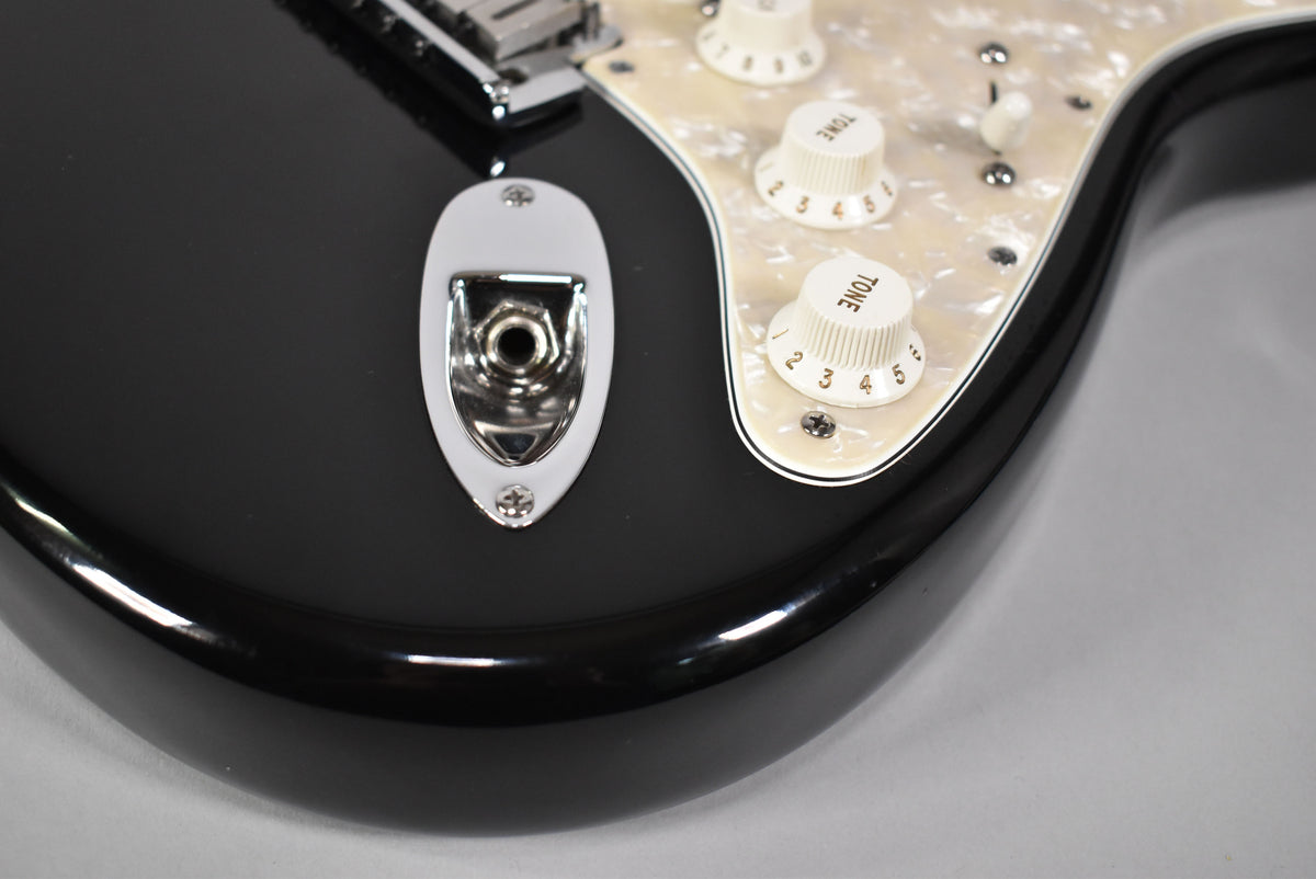 Close-up of the black guitar body's lower bout, showing the chrome output jack and three cream "Tone" knobs on a pearloid pickguard.