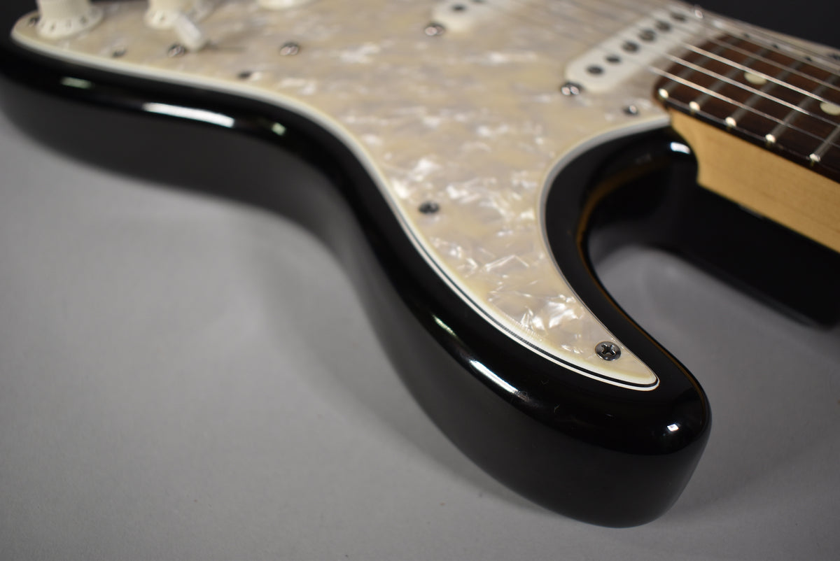 Close-up of a black guitar body with a pearloid pickguard, showing part of the neck and fretboard.
