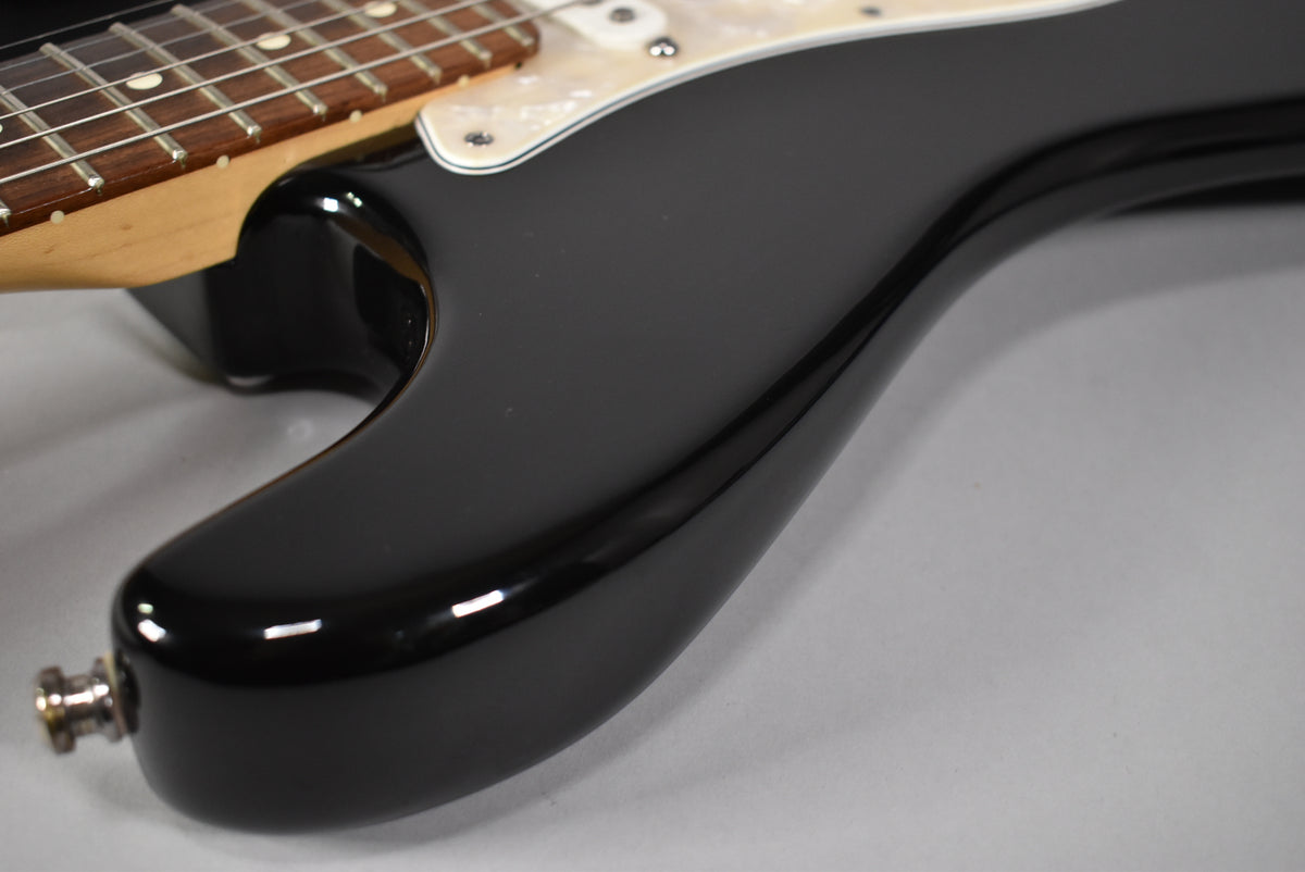 Close-up of the glossy black body from the lower bout, showing the output jack, pearloid pickguard, and rosewood fretboard.