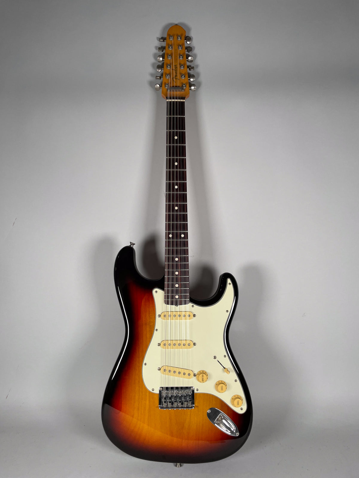 Full-length, front view of a sunburst 12-string electric guitar with a white pickguard, three cream single-coil pickups, and gold knobs.