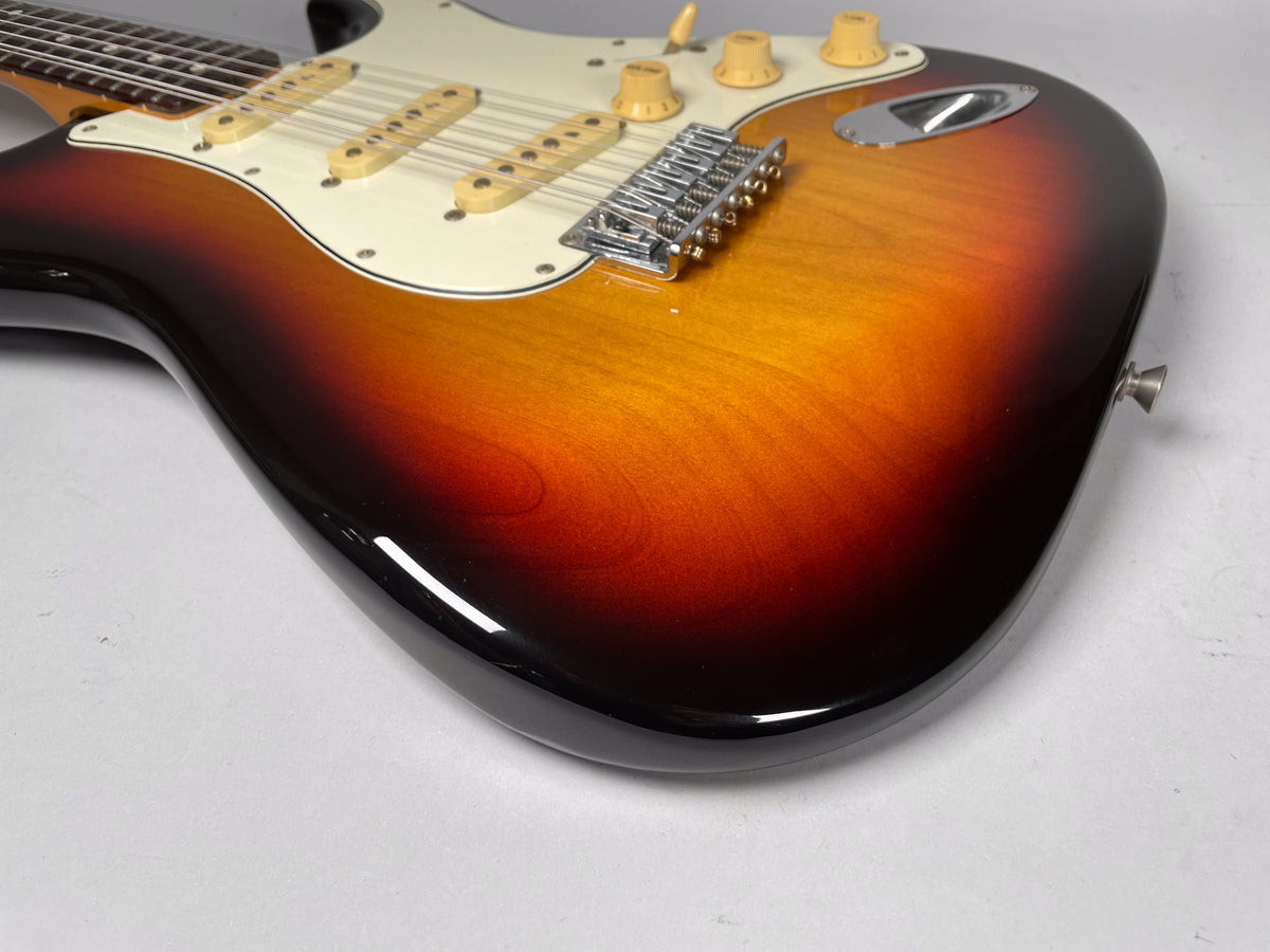 The sunburst 12-string electric guitar body, with a white pickguard and cream pickups, is angled to show the lower bout and controls.
