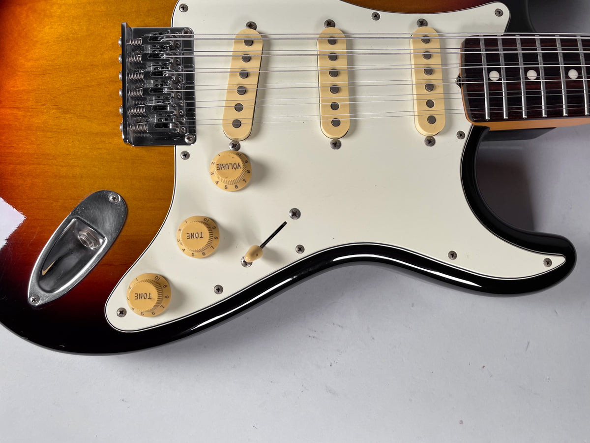 Close-up of the sunburst body, showing the white pickguard, three cream single-coil pickups, three cream control knobs, and tremolo bridge.