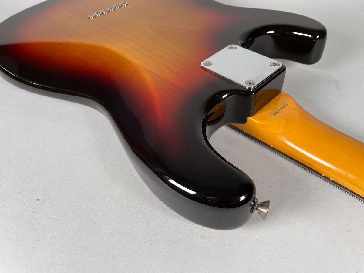 The guitar's sunburst body and neck joint are seen from the back, with a chrome neck plate and strap button, plus some wear on the lower horn.