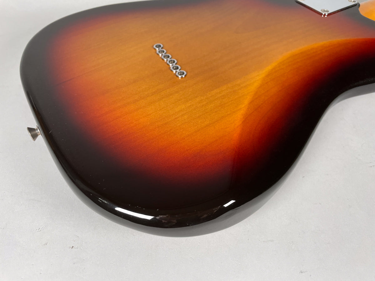 The sunburst guitar body's lower bout is shown from the back, revealing string-through ferrules and a ding on the bottom edge.