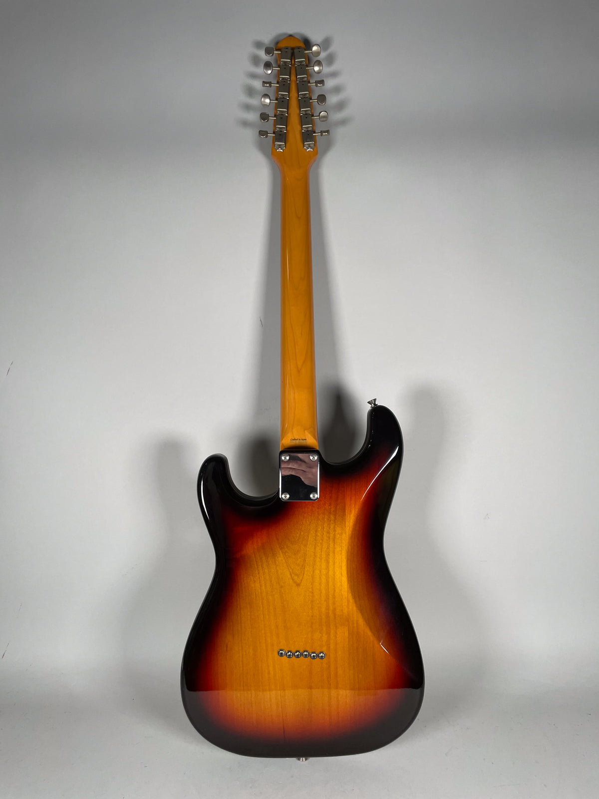 The back of a sunburst 12-string electric guitar, showing the neck plate, six string ferrules, and 12 tuners on the headstock.