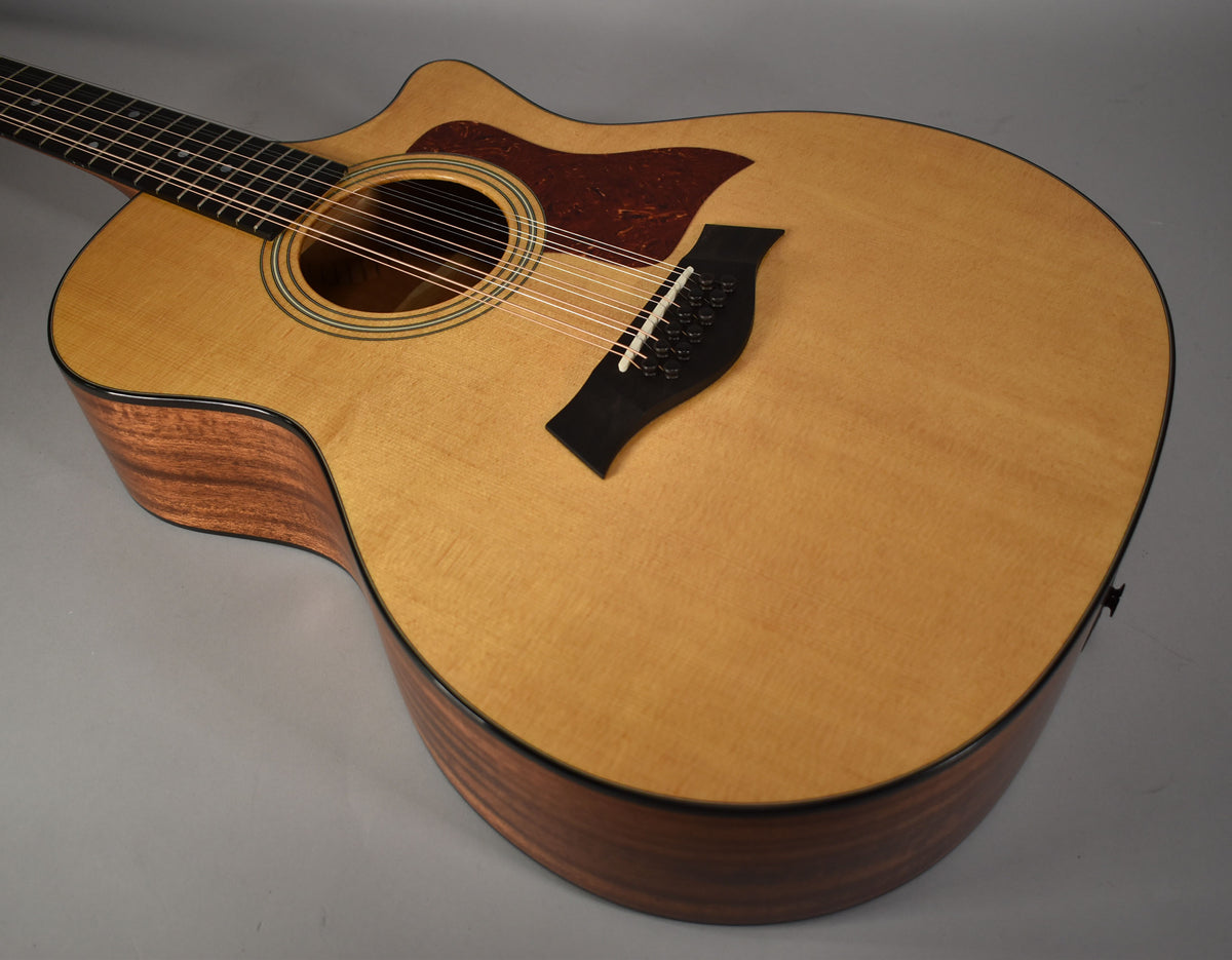 The natural finish 12-string acoustic guitar is angled from the upper left, showing the light wood top, dark wood sides, and black bridge.