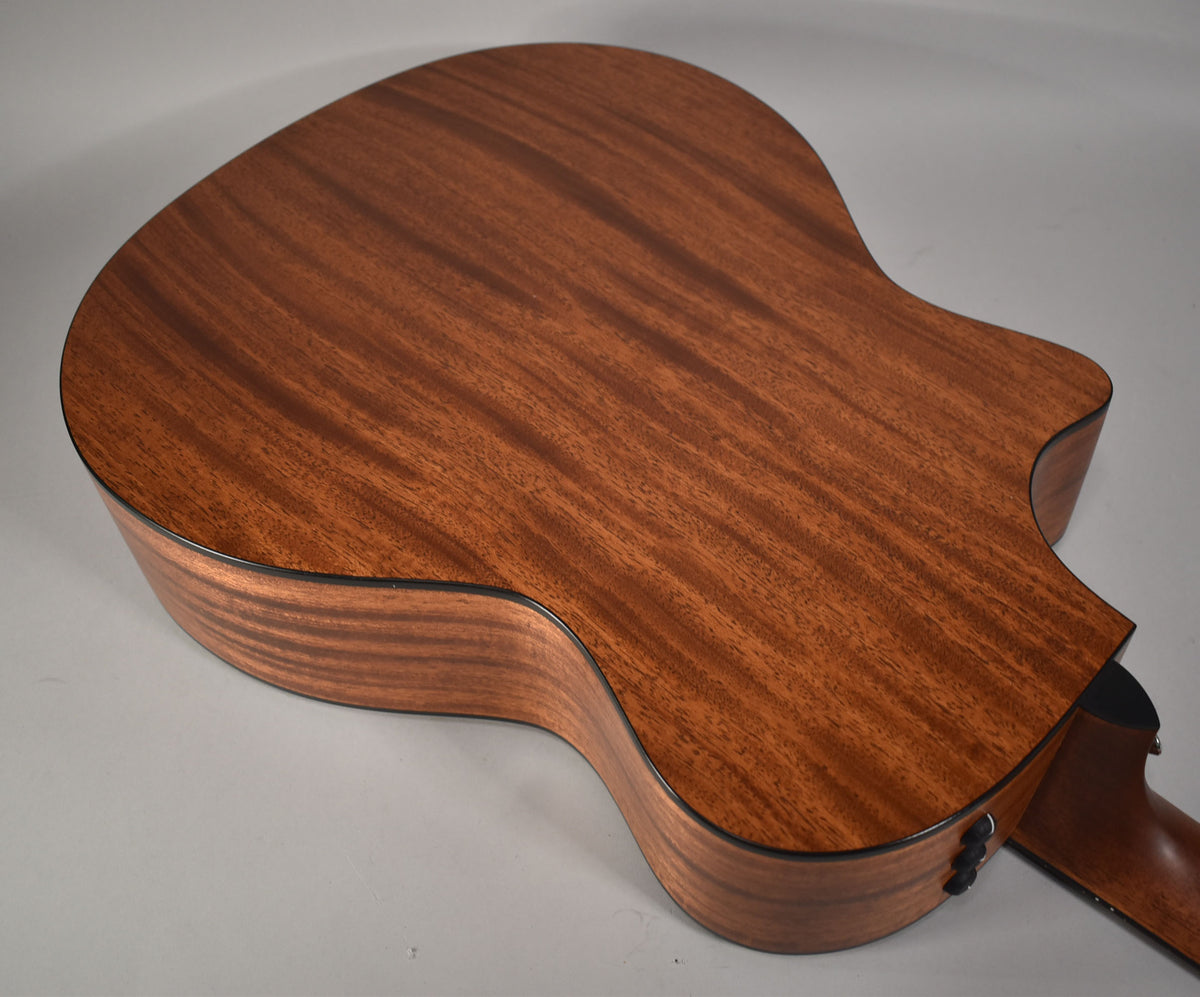 The guitar's back and side are visible, showing a natural, satin-finished mahogany with subtle wood grain and black binding.