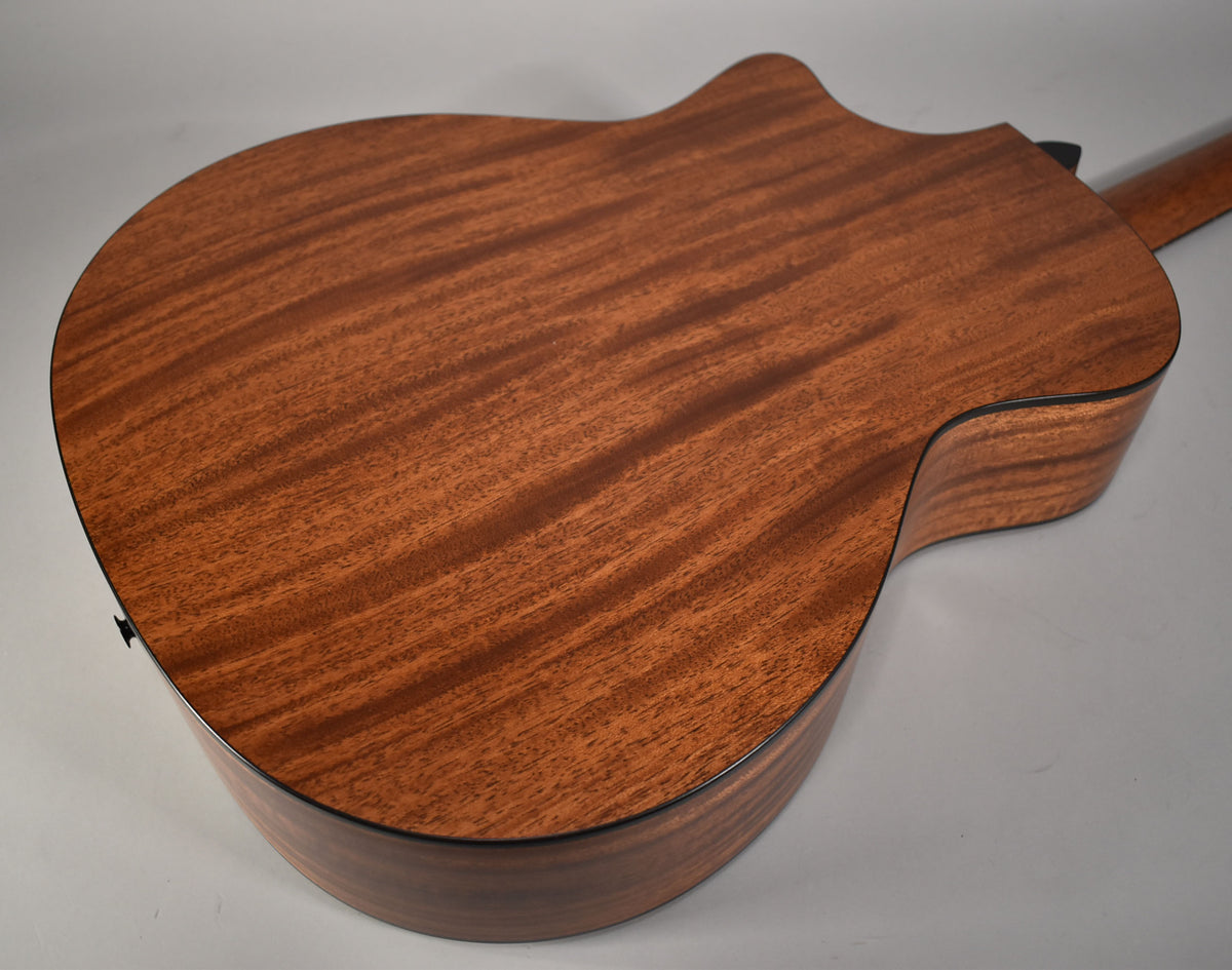 The guitar's back and side are visible, showing a natural reddish-brown wood grain with a satin finish and black binding.
