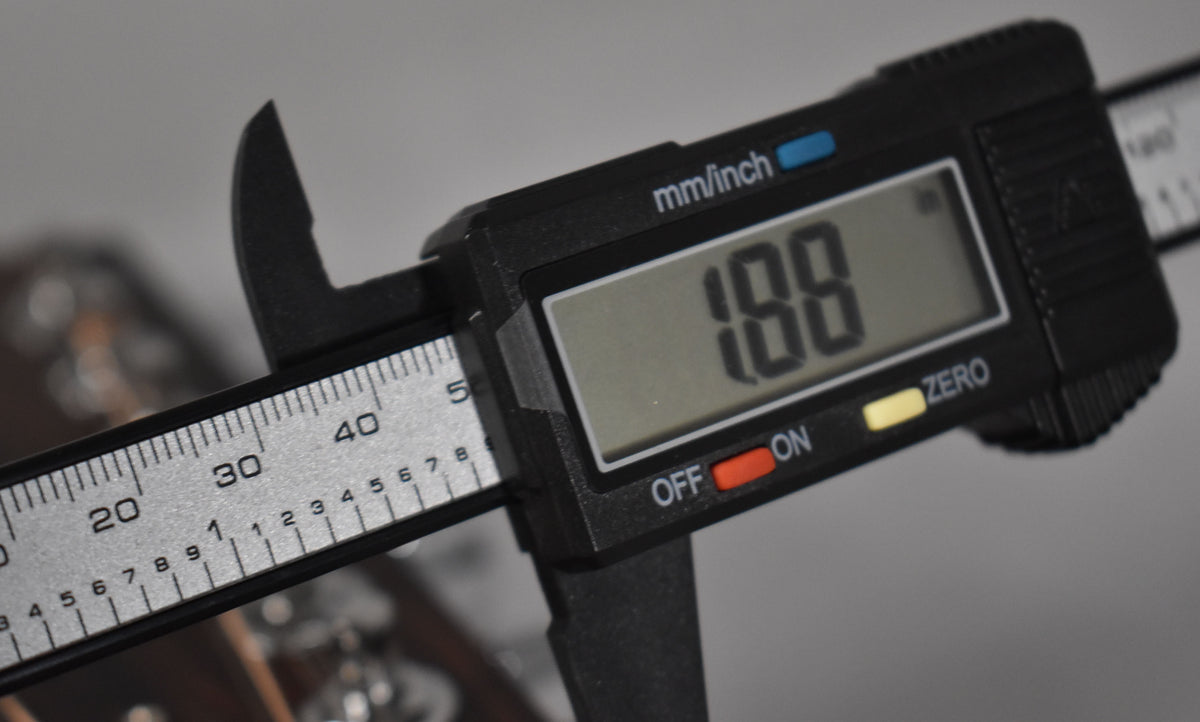A digital caliper measures the guitar's nut width, displaying "1.88" on its screen, with the "mm/inch" button visible.