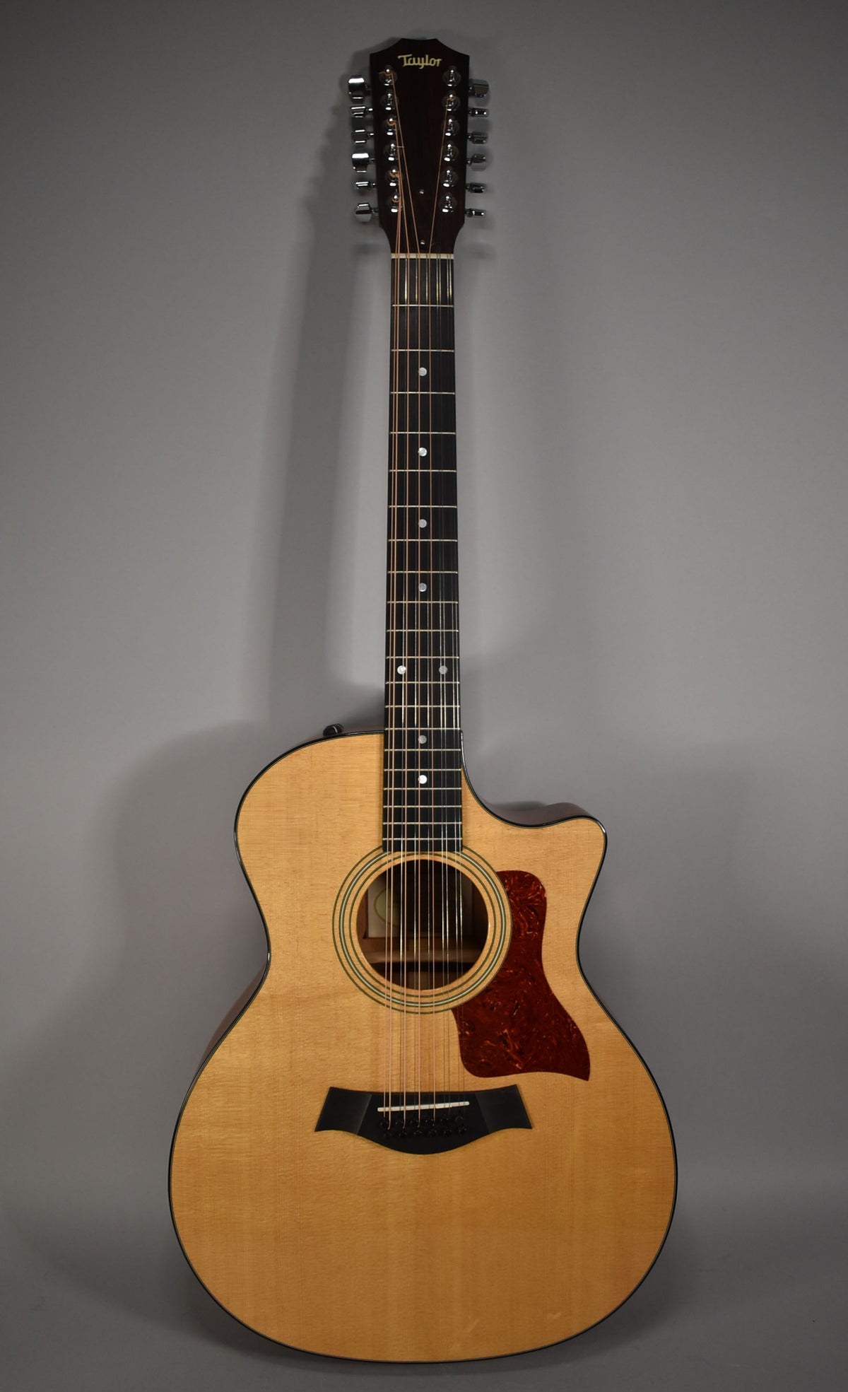 Full-front view of a natural finish 12-string acoustic-electric guitar with a cutaway body, dark pickguard, and black bridge.