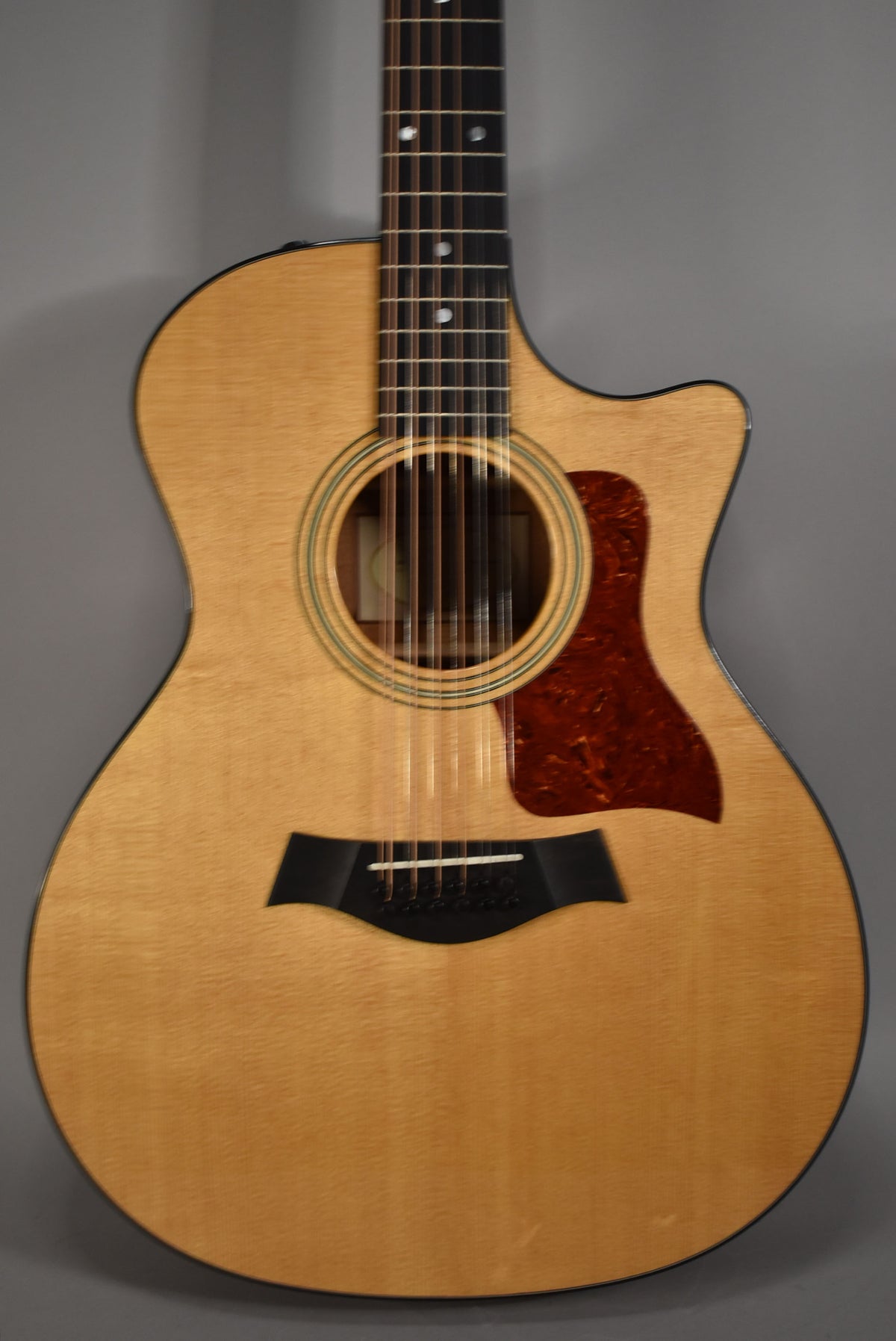 Full front view of a natural finish 12-string acoustic guitar with a tortoise shell pickguard and black bridge.