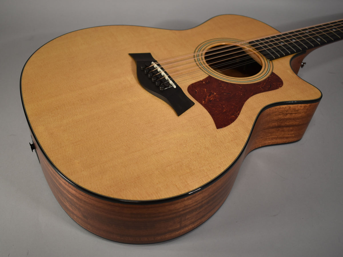 Upper body of a natural finish 12-string acoustic guitar, showing the light wood top, dark wood sides, and tortoise pickguard.