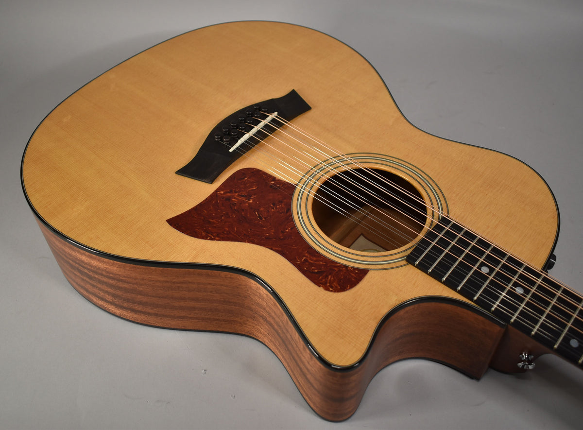 The 12-string acoustic-electric guitar's light wood top and dark wood sides are angled, showing the soundhole, pickguard, and bridge.