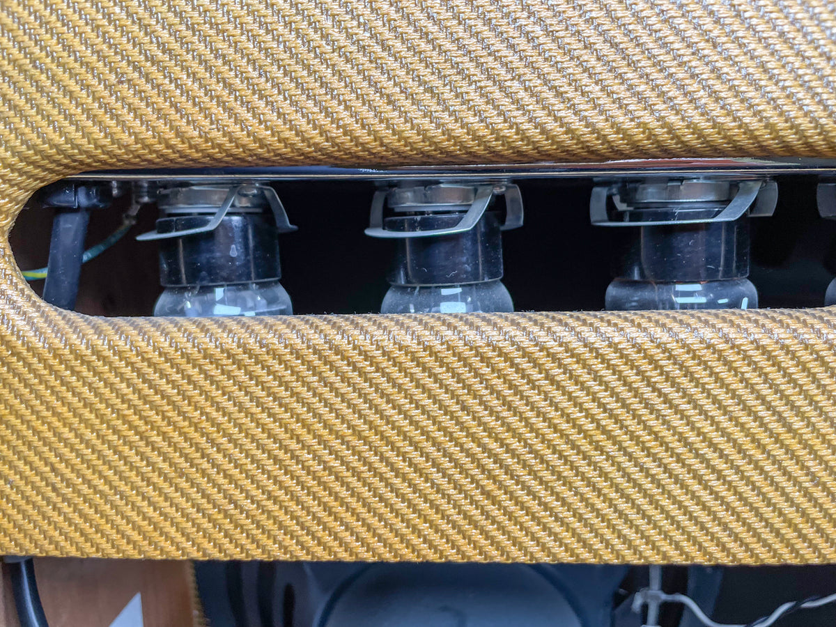 Close-up of three vacuum tubes with metal retainers, visible through a cutout in the tweed-covered top of the amp.
