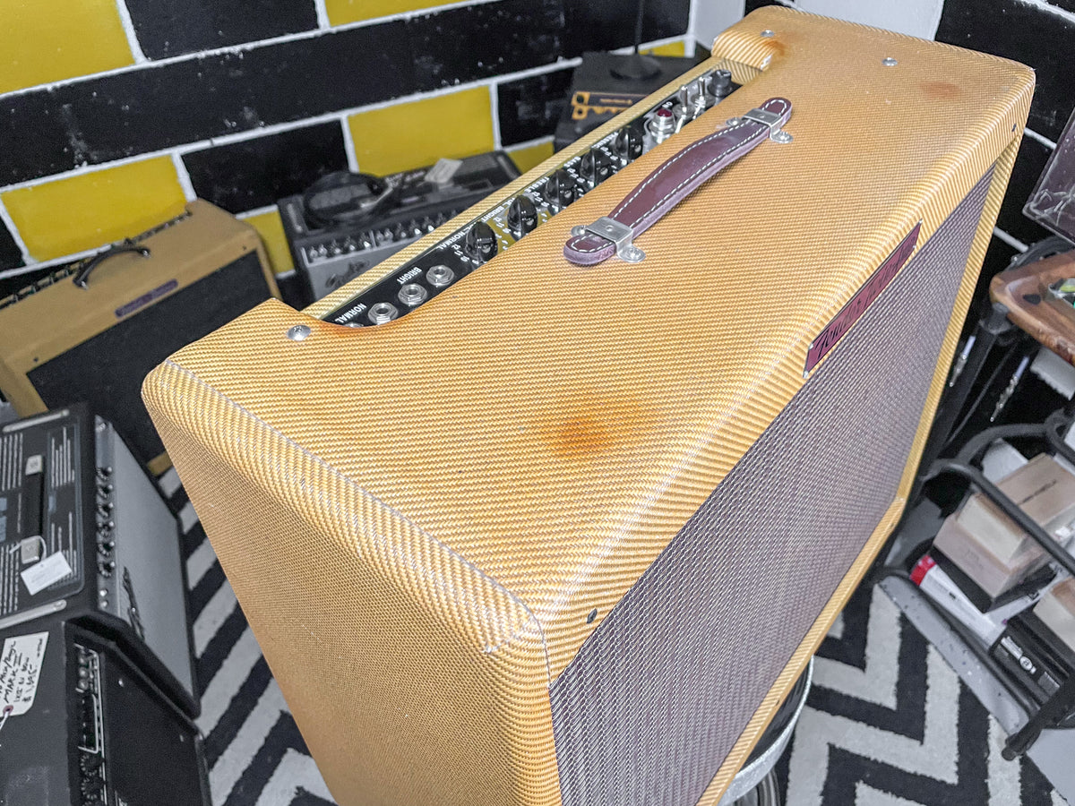 Angled view of a tweed combo amp with a brown leather handle, showing a dark stain on top and a dark grille cloth.