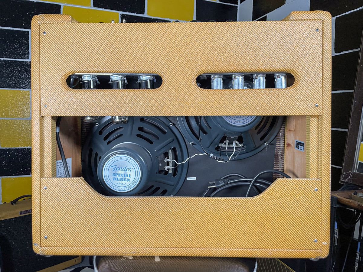Rear view of a tweed combo amp, showing two large speakers, internal wiring, and eight glowing vacuum tubes visible through a top vent.
