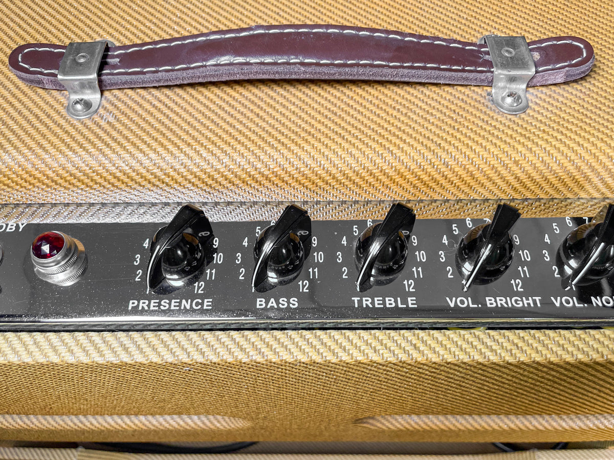Close-up of the amp's top, showing a brown leather handle, tweed covering, and the control panel with black knobs and a red jewel light.