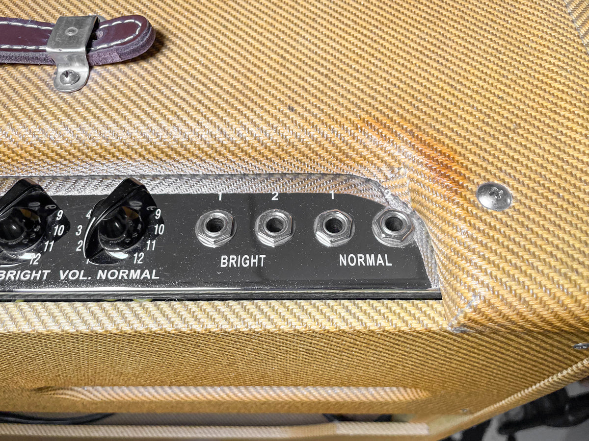 Close-up of the amp's tweed top, showing a brown leather handle, black control panel with four inputs, two volume knobs, and a rust-colored stain.