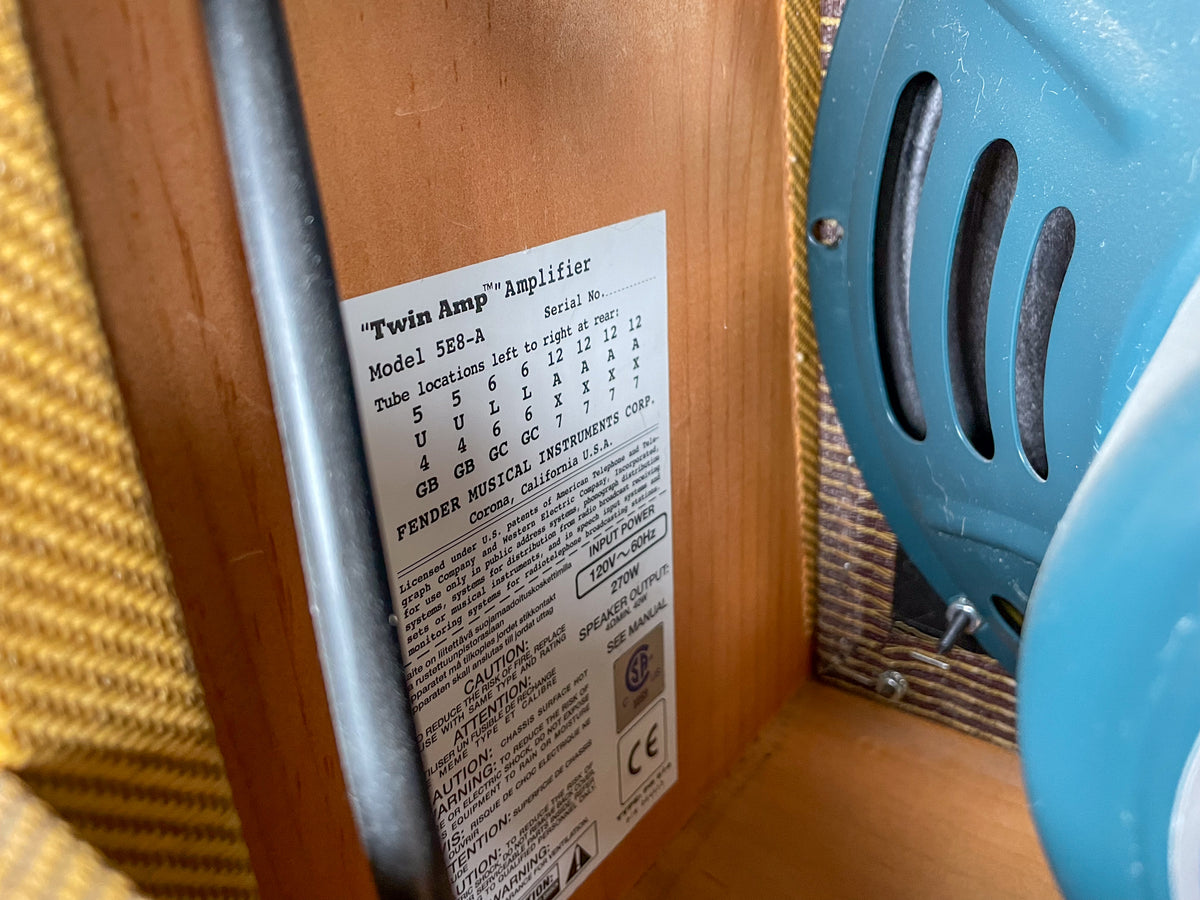 Close-up of the amp's rear, showing a white label with specifications and a light blue speaker with three vertical slots.