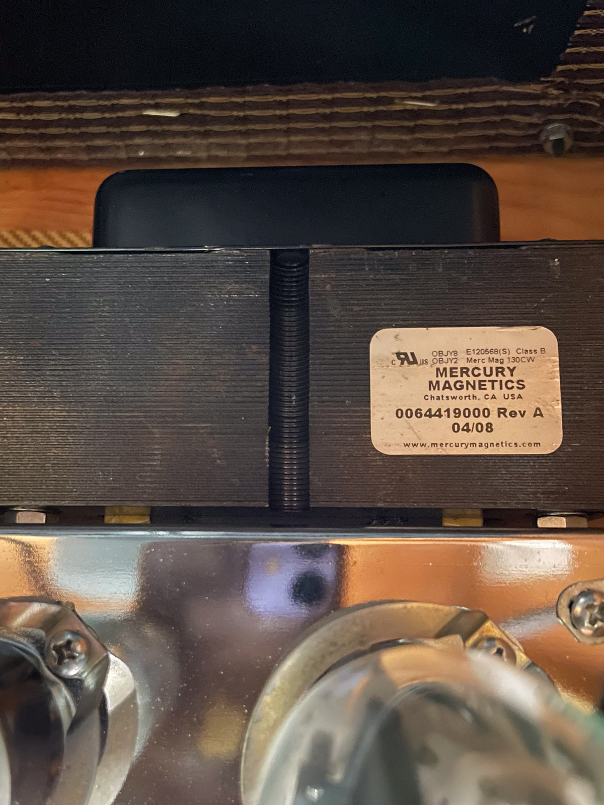 Close-up of the amp's rear, showing a black transformer with a white Mercury Magnetics label, above a reflective chrome chassis and vacuum tubes.