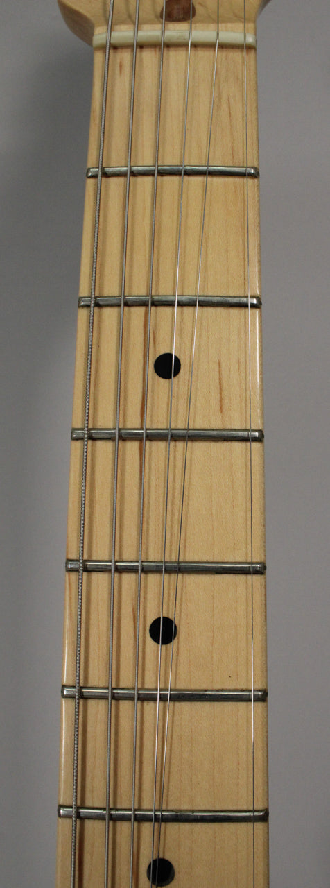 Close-up of the maple fretboard, showing the nut, first few frets, and black dot inlays on a light wood grain.