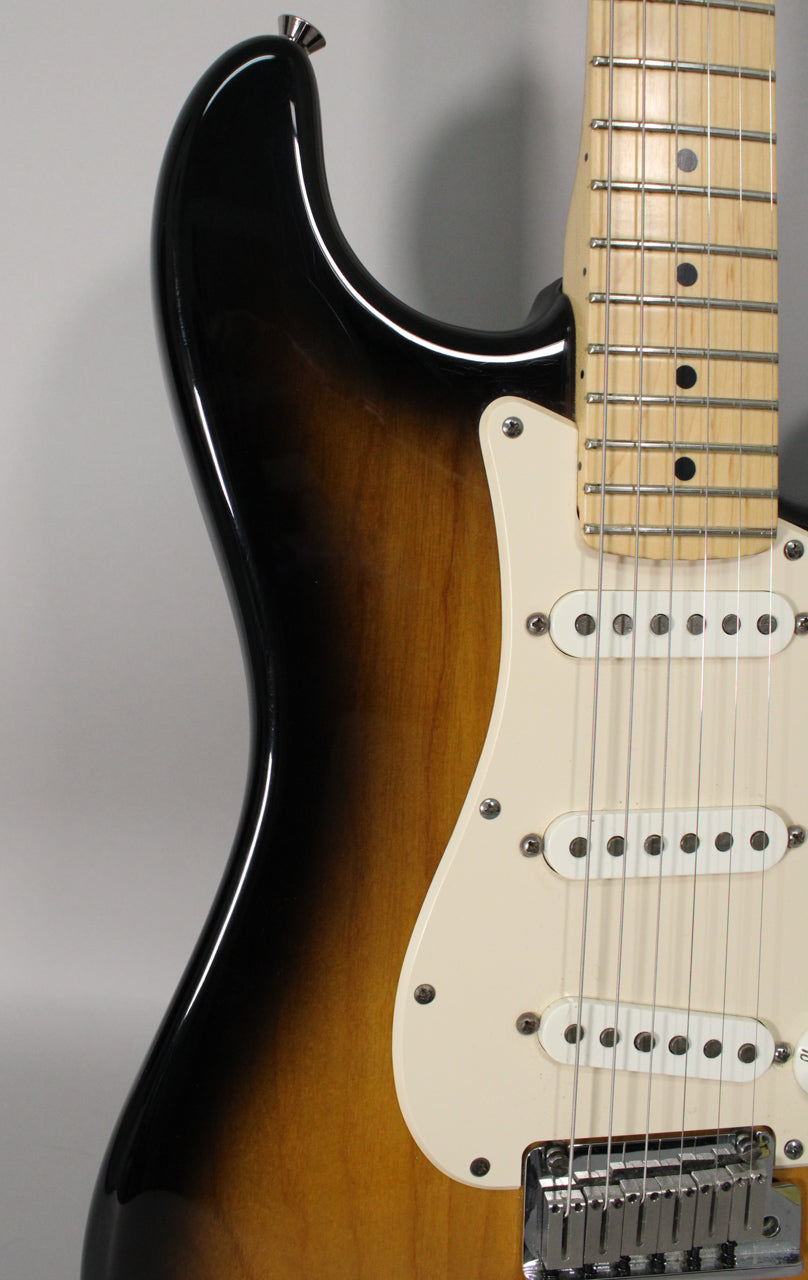 The upper body of a sunburst Stratocaster, showing the maple fretboard, cream pickguard, and three single-coil pickups.