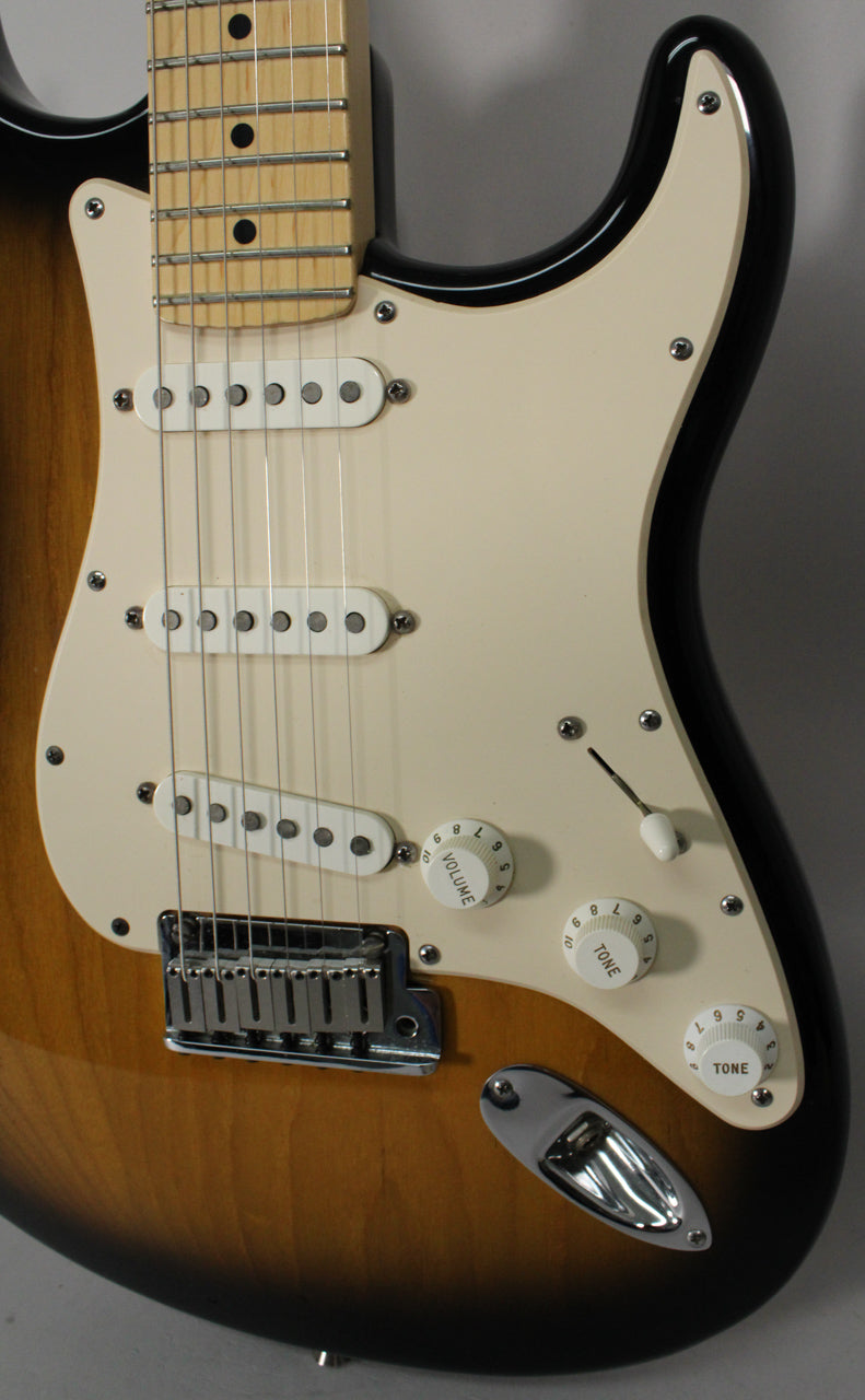 The guitar's body, in 2-color sunburst, is angled to show the cream pickguard, three single-coil pickups, and control knobs.