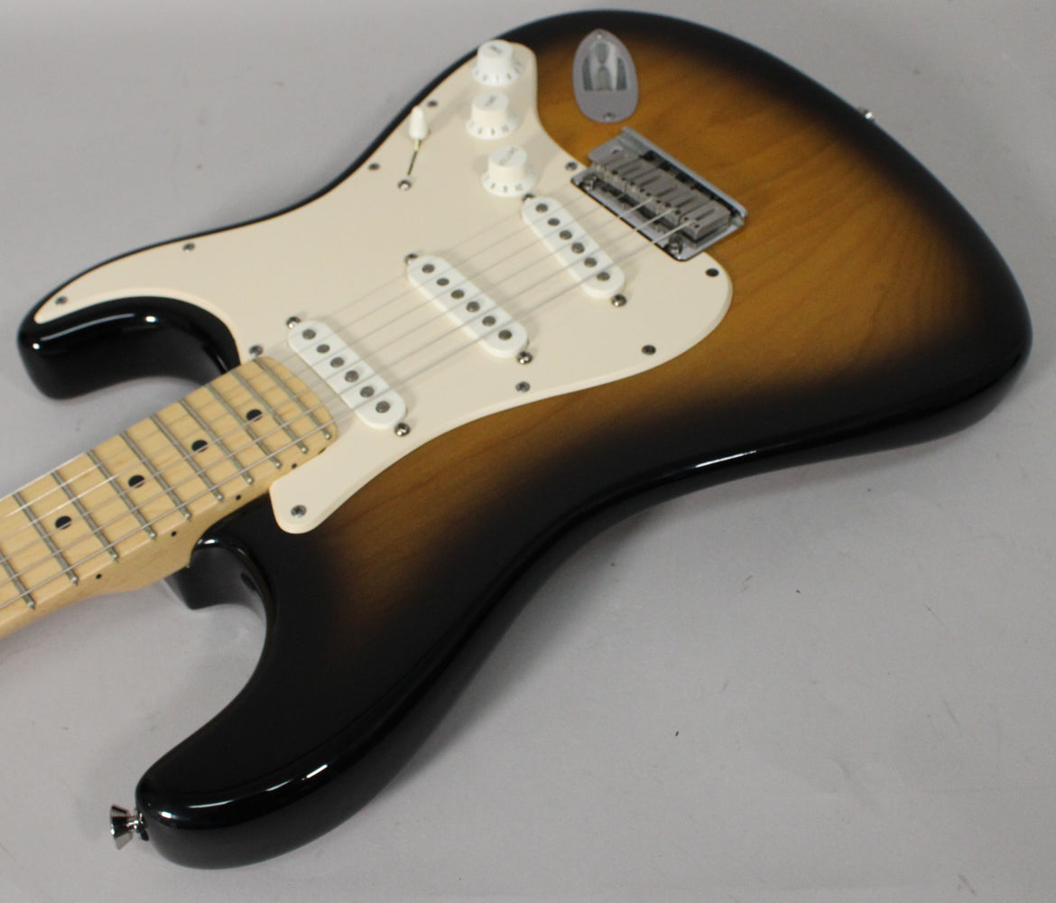 The Stratocaster's 2-color sunburst body and white pickguard are shown from the upper bout, with a maple fretboard visible.