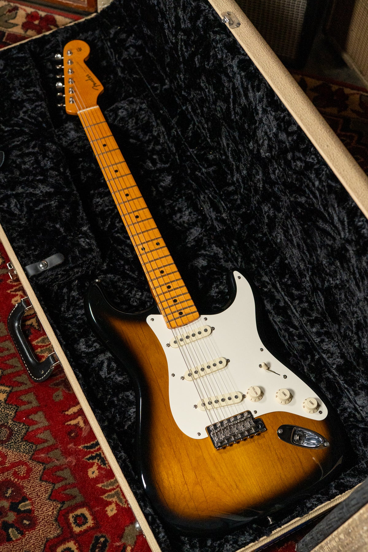The sunburst Stratocaster is angled in its open case, showing its maple neck, white pickguard, and three single-coil pickups.
