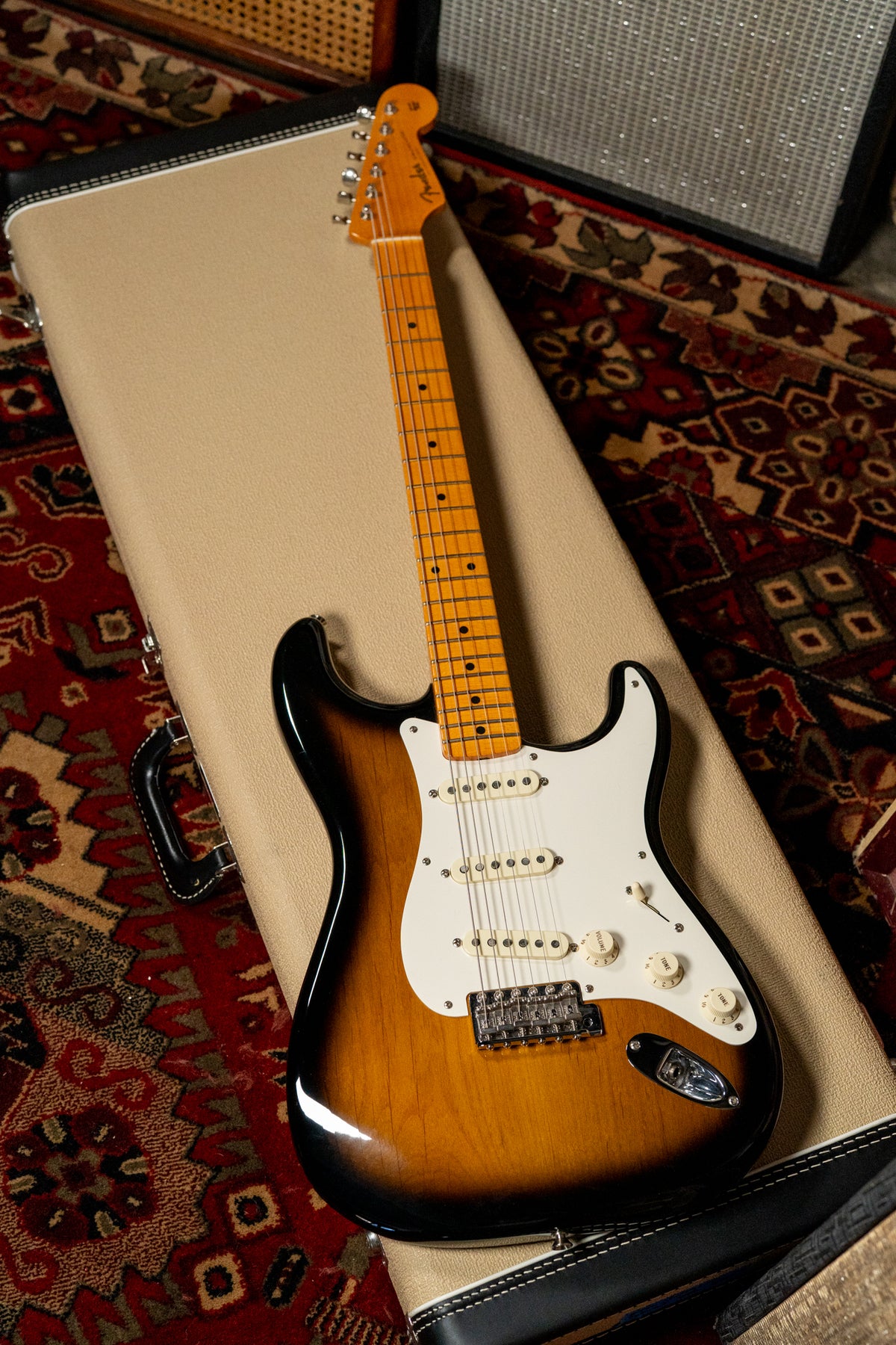 Sunburst Stratocaster with a maple neck and white pickguard, resting on a beige hardshell case with a black handle.