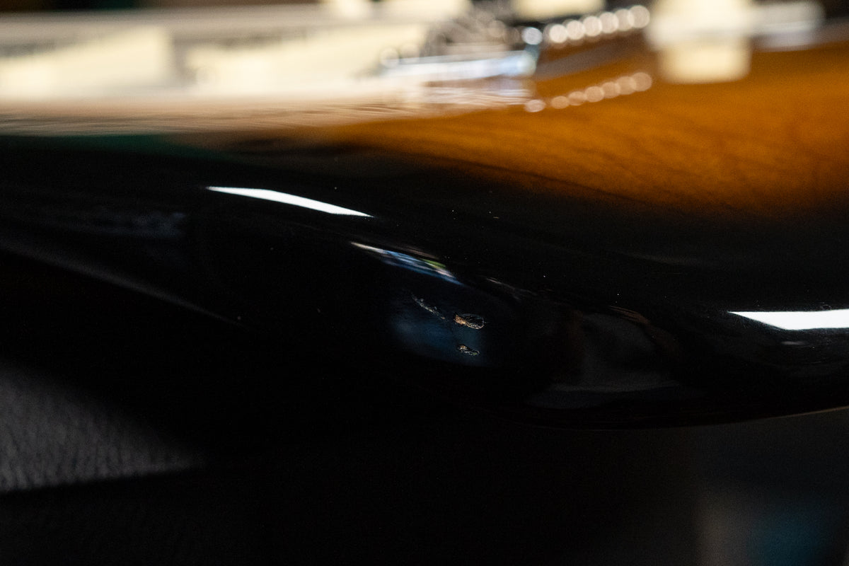Close-up of the guitar's lower bout, showing the glossy black edge of the sunburst finish with two small chips revealing lighter wood.