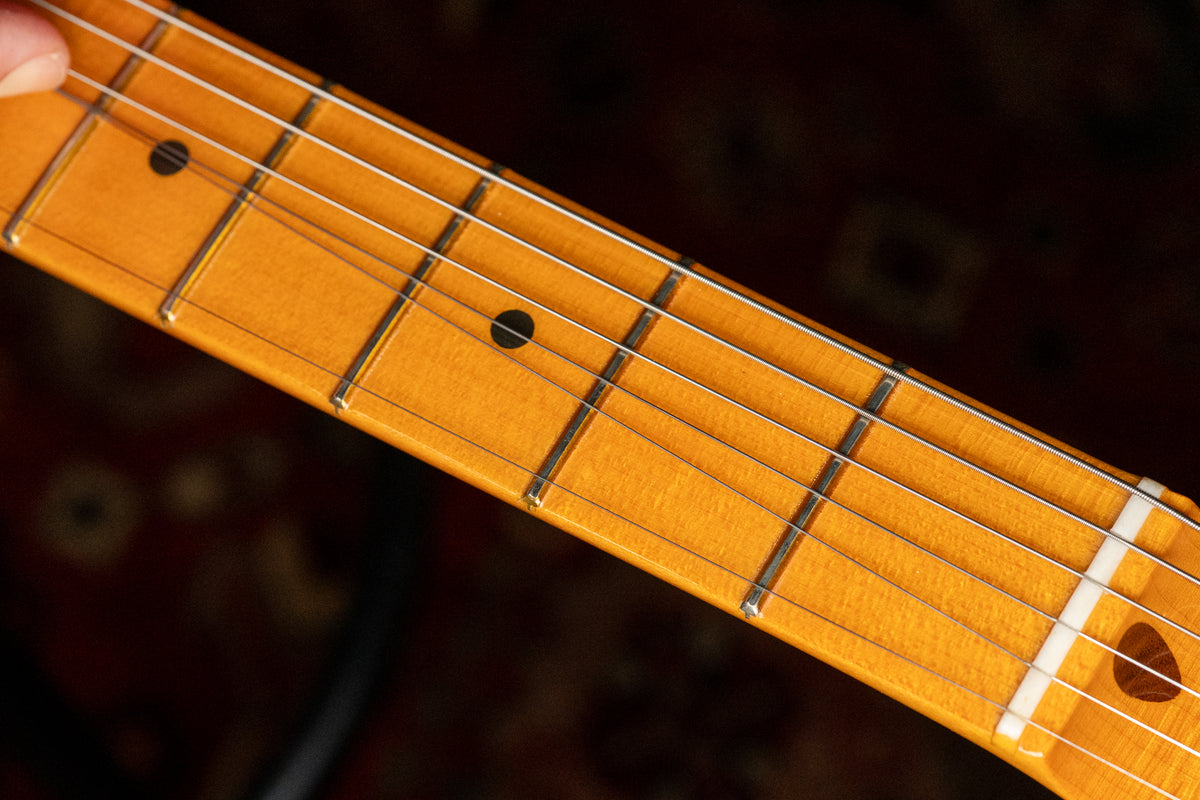Close-up of the maple fretboard, showing frets 1-7, black dot inlays, and the white nut with a small chip near the low E string.