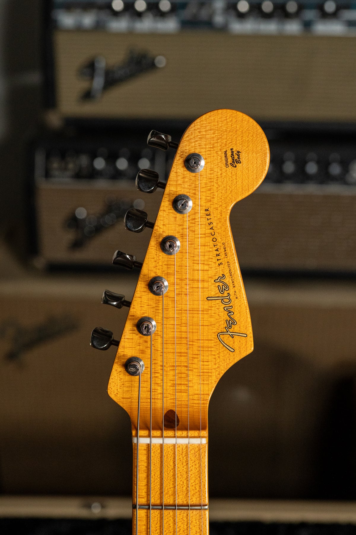 The guitar's headstock, with a light amber finish and dark grain, is angled slightly left, showing six dark tuning pegs.