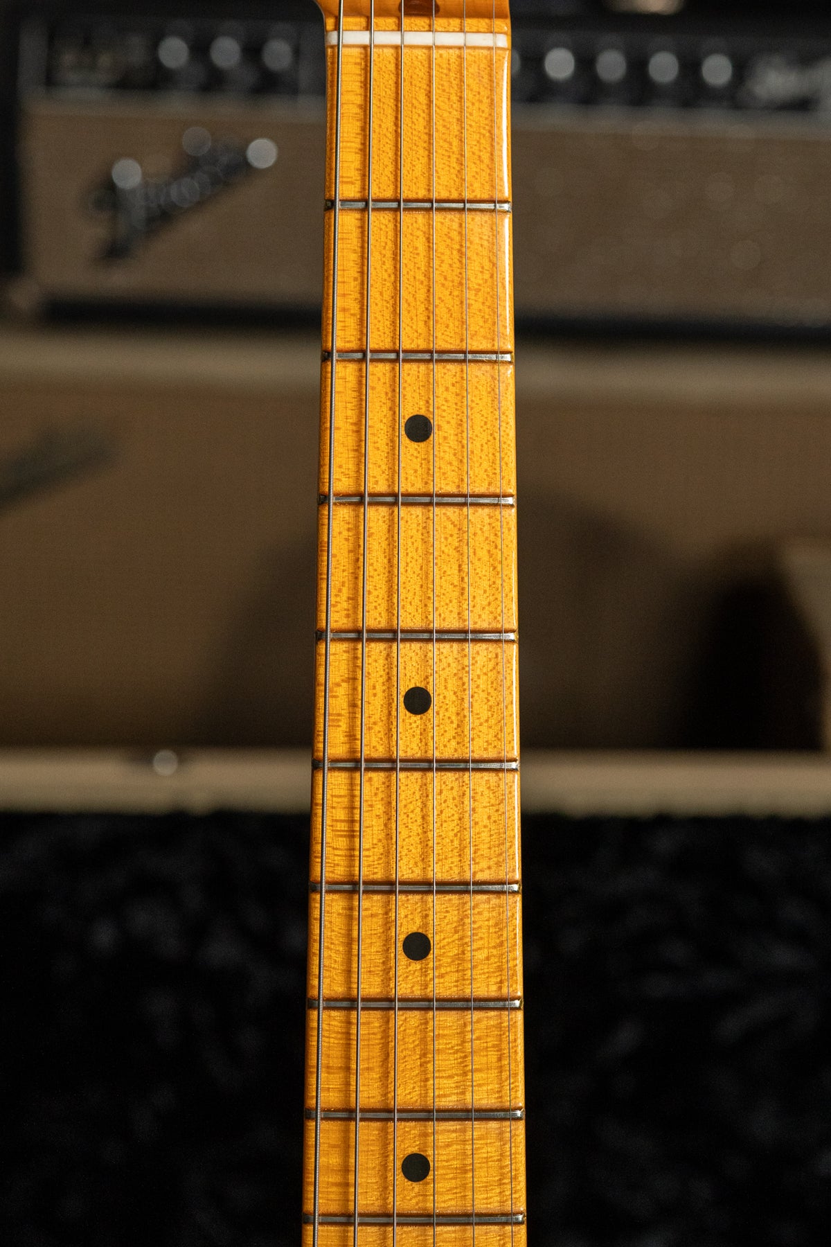 Close-up of the guitar's maple fretboard, showing dark dot inlays, frets, and visible wood grain, with a white nut at the top.