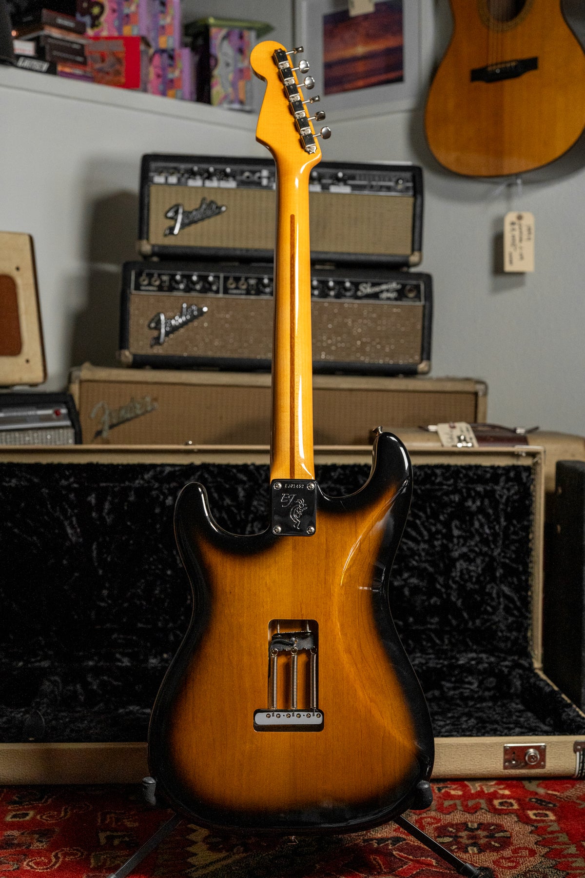 The guitar's two-tone sunburst body and maple neck are viewed from the back, showing the tremolo cavity and neck plate.