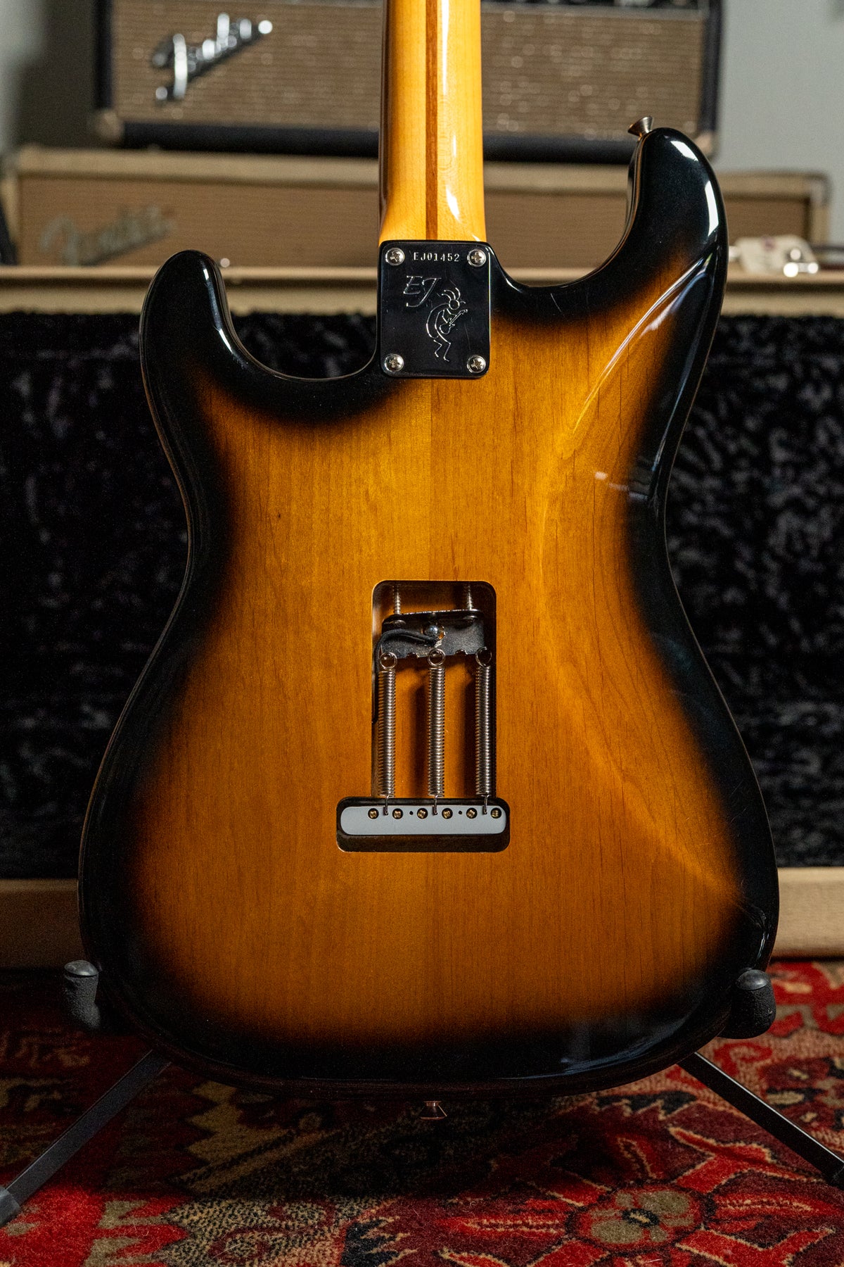 The guitar's two-tone sunburst back shows a neck plate with a figure, and a tremolo cavity with three springs and a white cover.