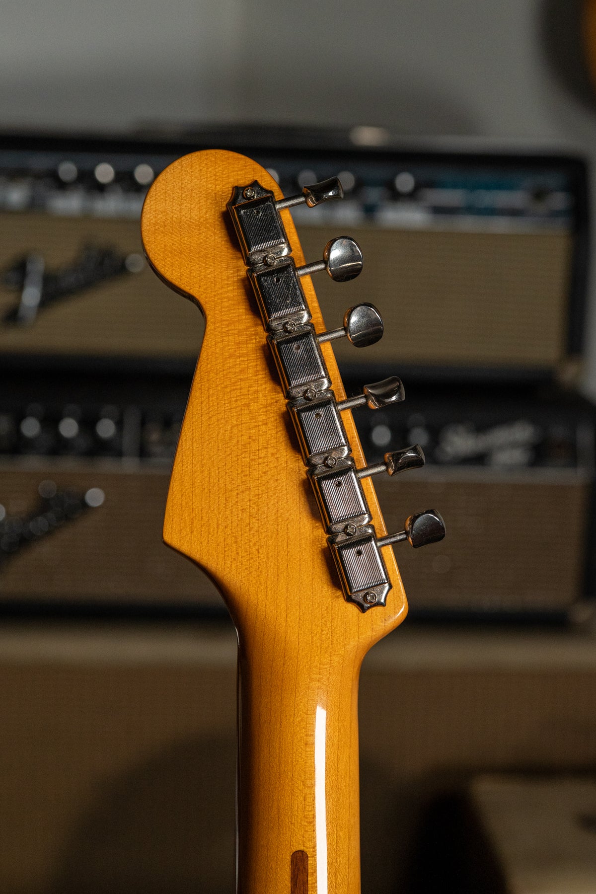 The guitar's headstock and neck are viewed from behind, showing six chrome tuners on the light amber-finished wood.