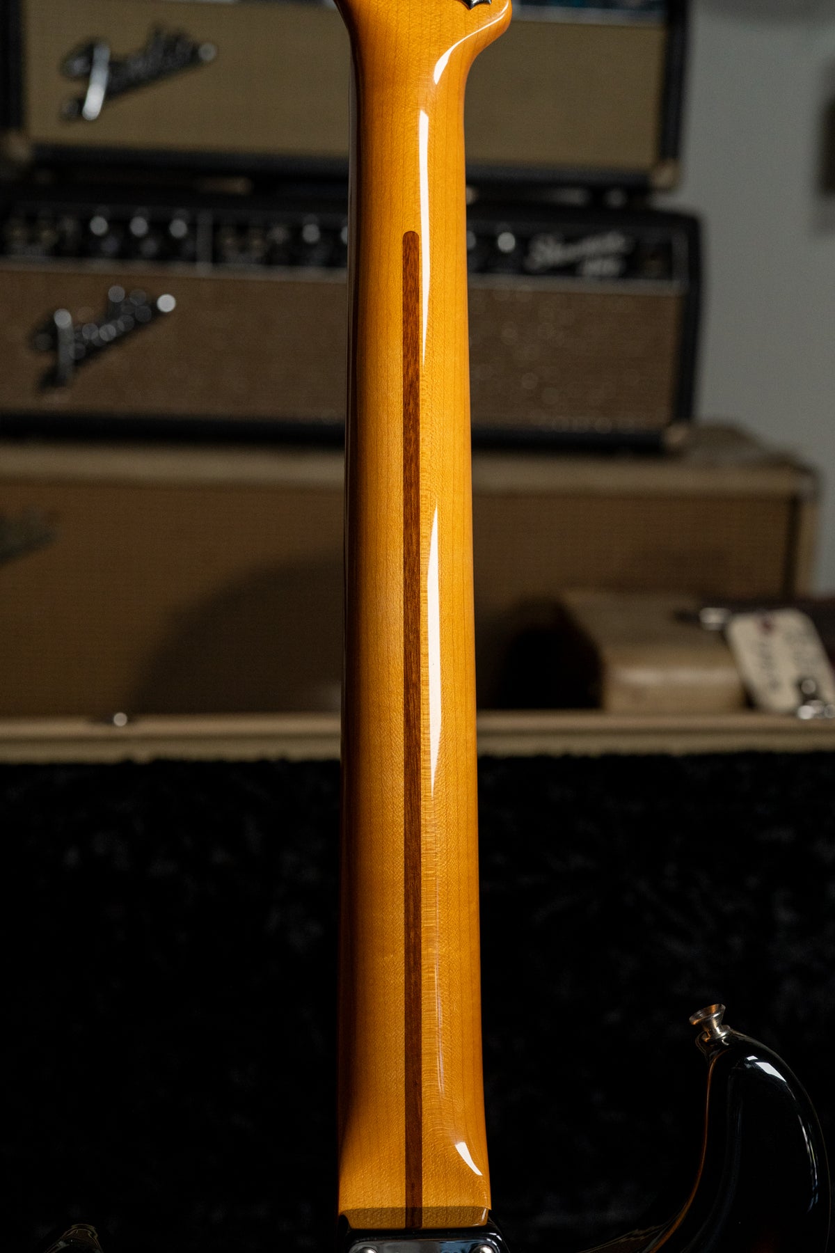 The guitar's glossy amber neck, with a dark wood skunk stripe, is viewed from the back, showing light wear near the heel.