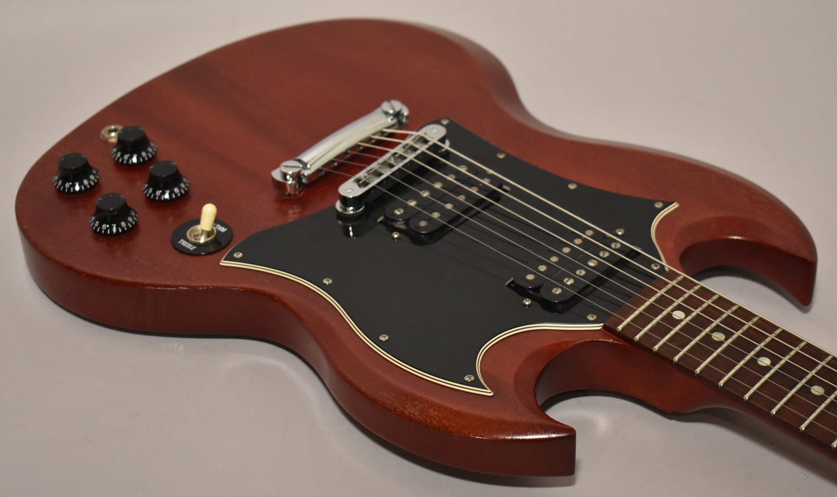 Close-up of the worn cherry SG's body, showing the black pickguard, two humbuckers, four black knobs, and a cream toggle switch.