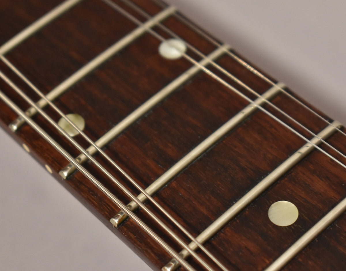 Close-up of the dark rosewood fretboard with light fret markers and frets, showing light wear on the lower frets.