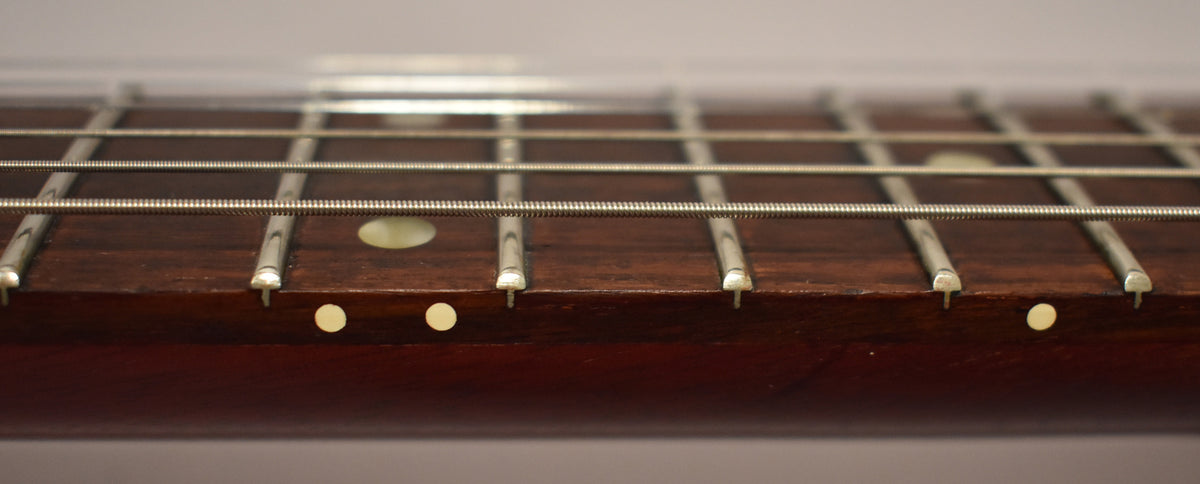Close-up of the dark cherry fretboard and frets, showing light wear and small cream dot inlays on the side and top.