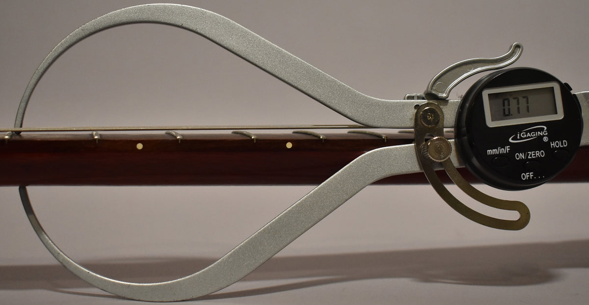 A digital caliper measures the guitar's dark cherry fretboard and frets, displaying "0.77" on its screen.
