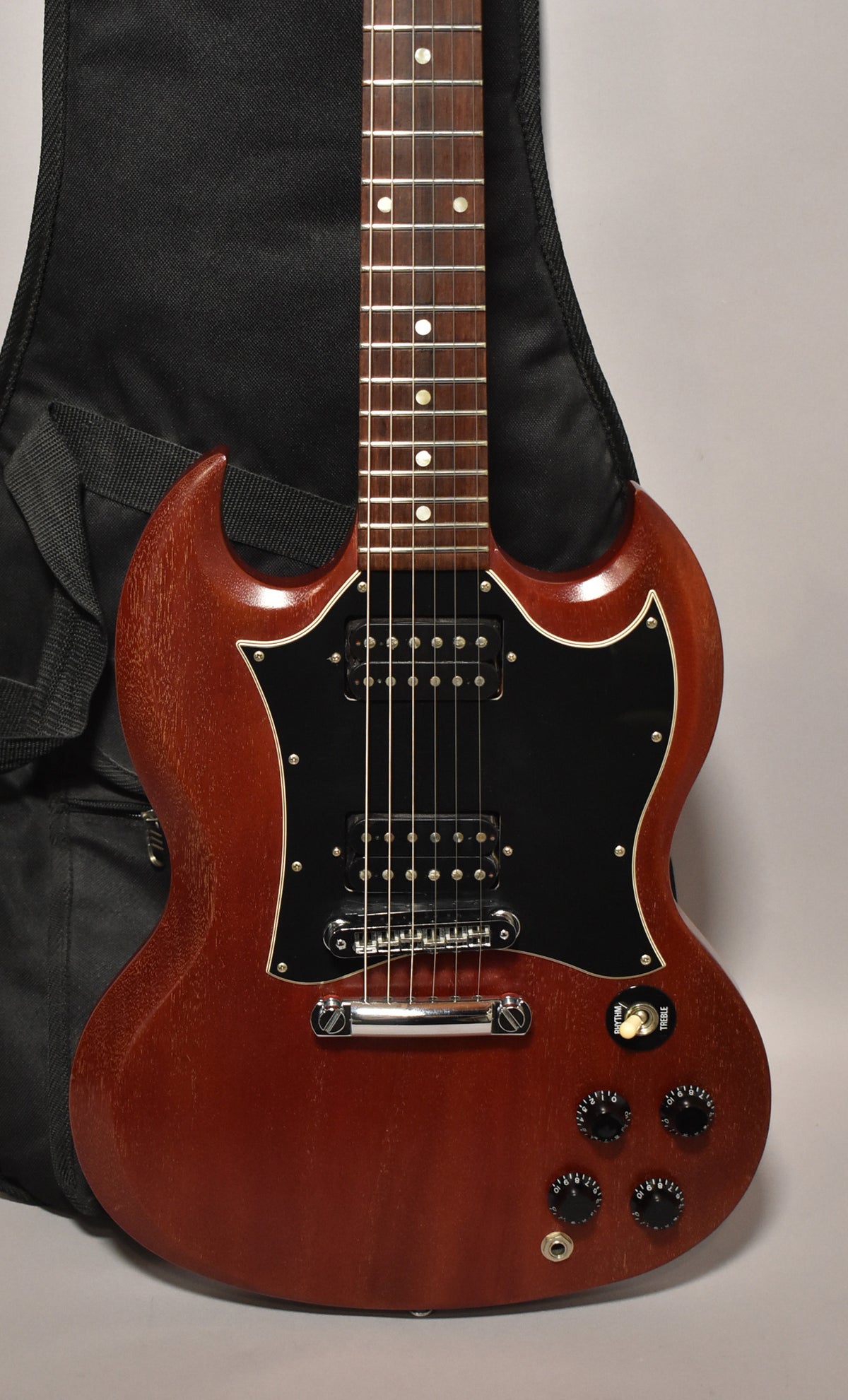Full view of a cherry red SG with a worn, faded finish, black pickguard, two humbuckers, and four black control knobs.