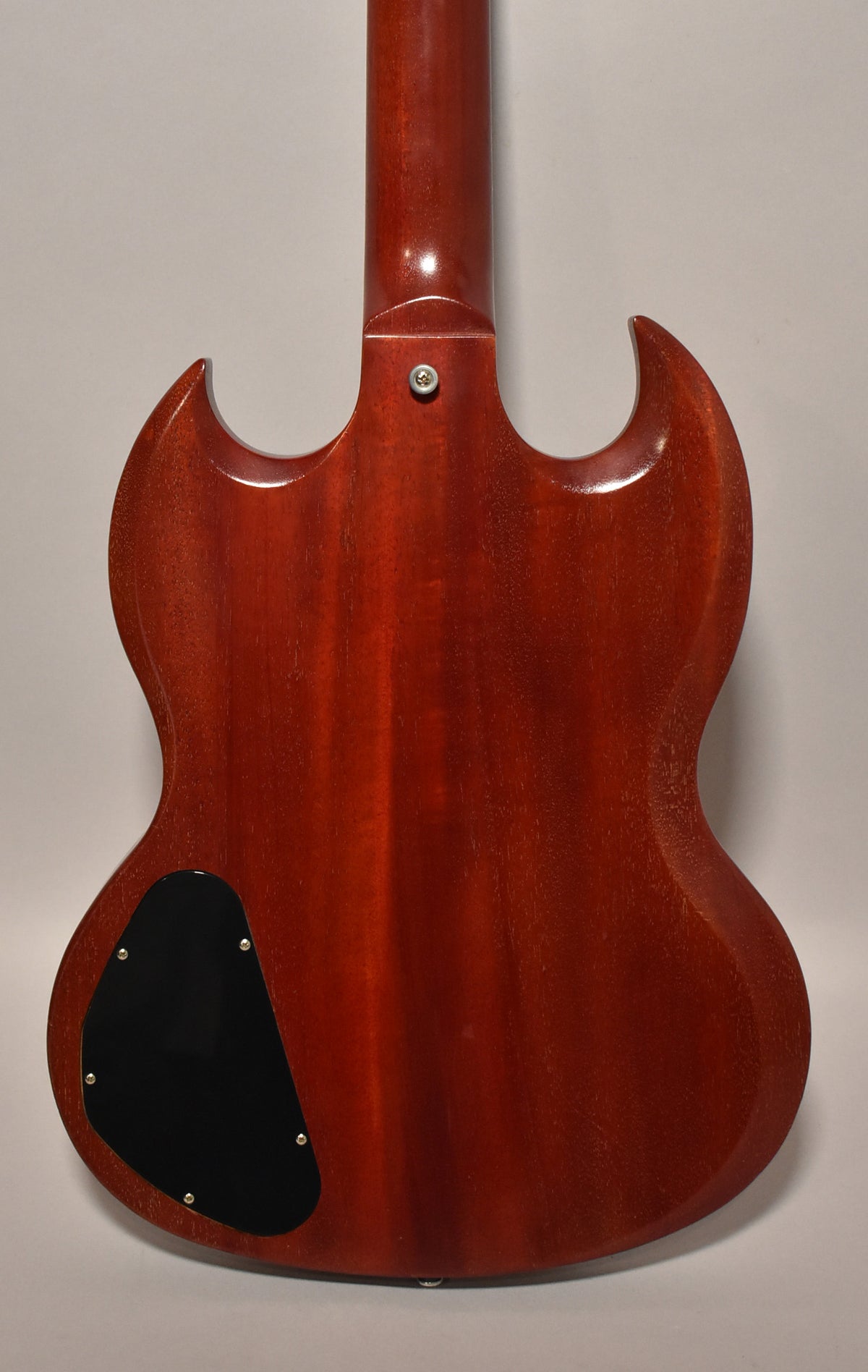 The back of a cherry red SG guitar, showing a black control plate and a worn, faded finish with some checking.